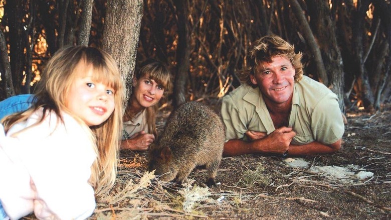 Bindi, Terri, and Steve Irwin posing on the ground with a quokka.