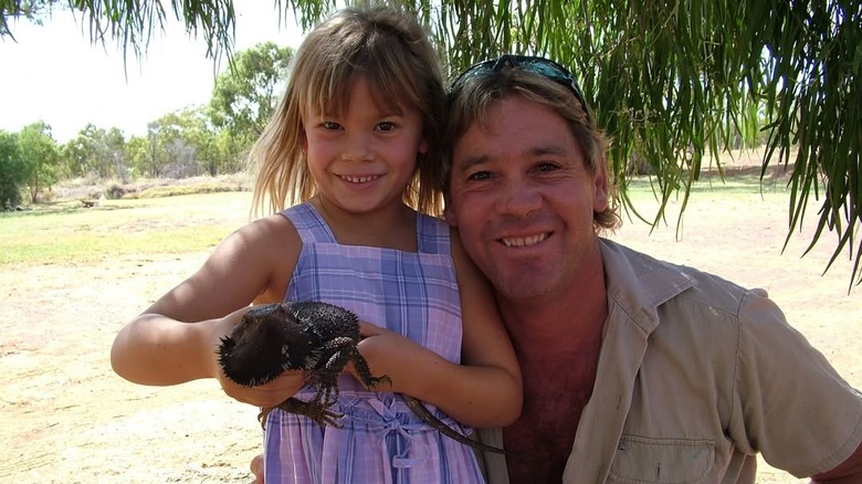 Steve Irwin and Bindi Irwin posing with a bearded lizard on a beach.