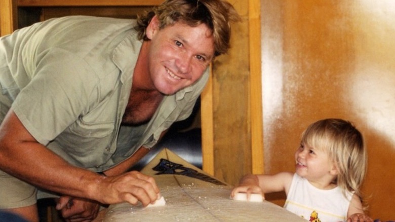 Bindi Irwin helping Steve Irwin sand a surfboard.