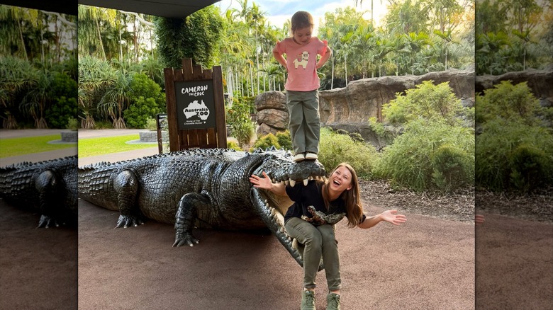 Bindi Irwin poses in a crocodile statue's mouth with Grace on top