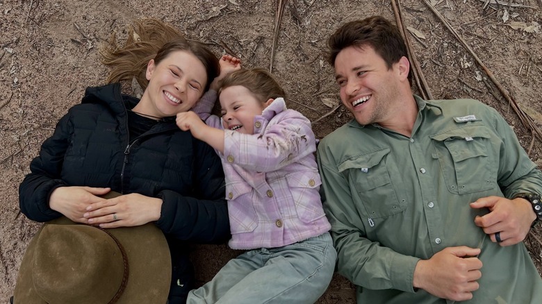Bindi Irwin smiles with daughter Grace and husband Chandler Powell on the ground