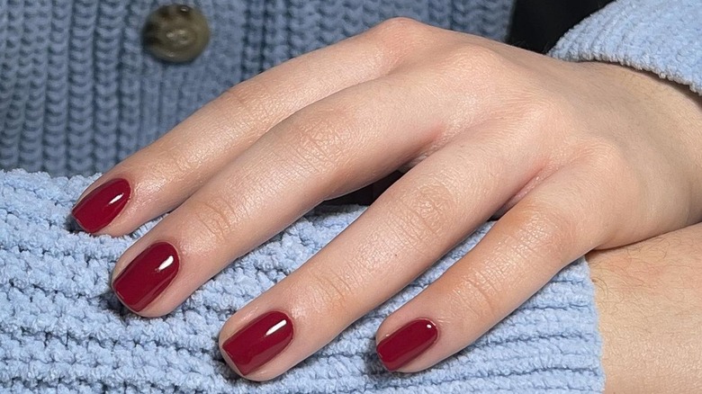 hand on blue cardigan red nails