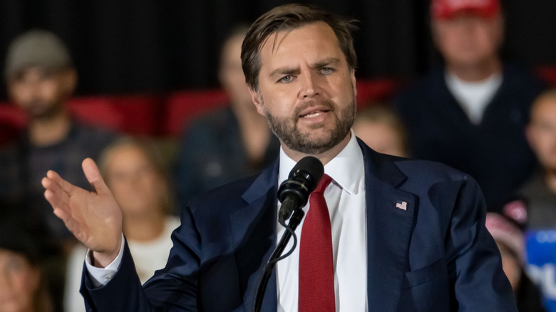 JD Vance speaking in front of a microphone in a navy suit