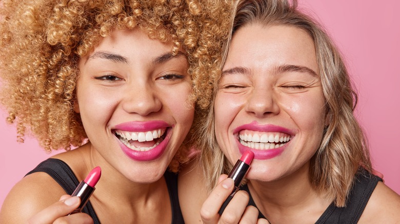 Two women smiling and applying lipstick