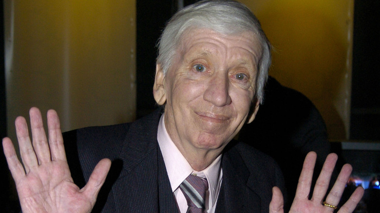 Bob Denver smiling and holding his hands up in a black suit
