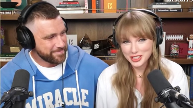 Travis Kelce smiling as Taylor Swift speaks during podcast interview