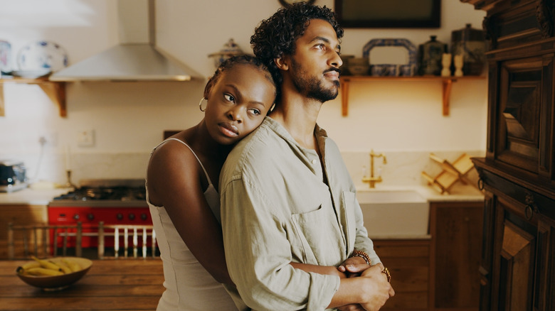 Couple holds one another, looks out with sad expression