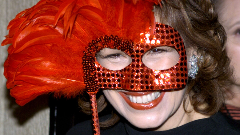 Joy Behar smiling with a red feather mask