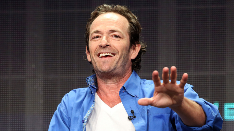 Luke Perry smiling, raising hand