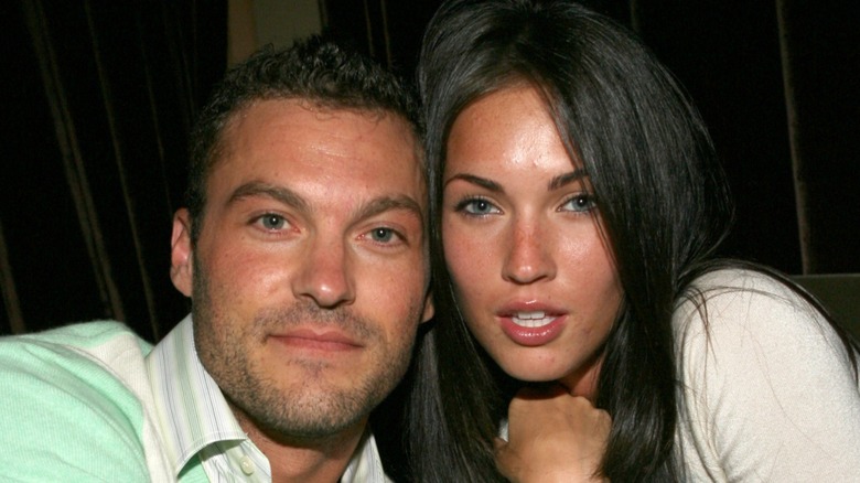 Brian Austin Green in a green shirt next to Megan Fox in a white shirt leaning on each other's heads.