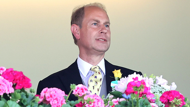 Prince Edward stands in a horse-racing box surrounded by flowers