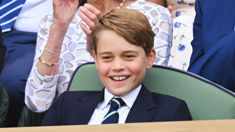 Prince George smiles as he watches a sports match from a seated arena