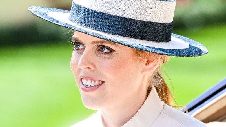 Princess Beatrice smiles and wears a striped hat in an outdoor setting