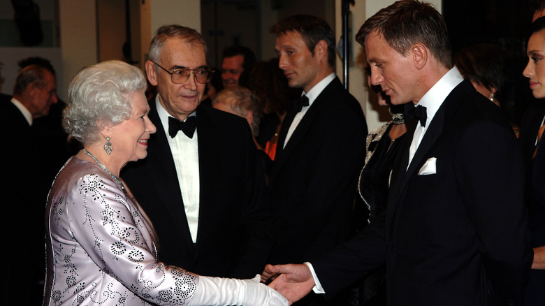 Queen Elizabeth II shaking hands with Daniel Craig with Mads Mikkelsen in the background