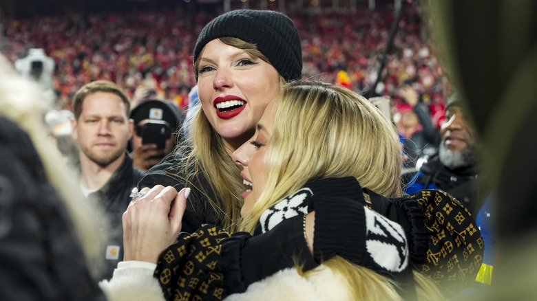 Taylor Swift hugs Brittany Mahomes at a Chiefs game in the stadium while Swift wears a Louis Vuitton hoodie.