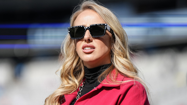 Brittany Mahomes looking confused while wearing sunglasses and a red jacket