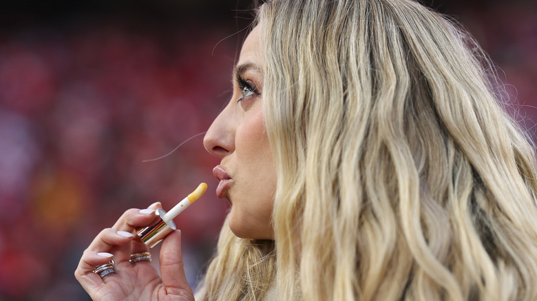 Brittany Mahomes putting on lip gloss while making a silly face