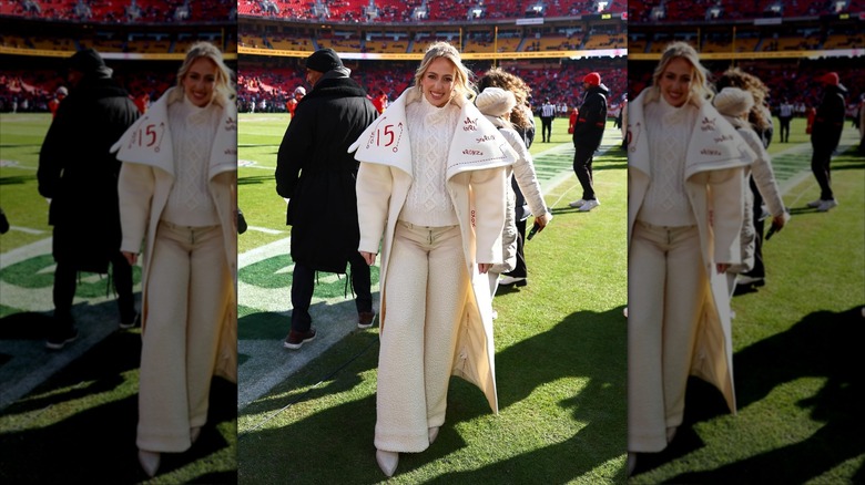 Brittany Mahomes in an all white outfit, including a large white and red coat, on the side lines.
