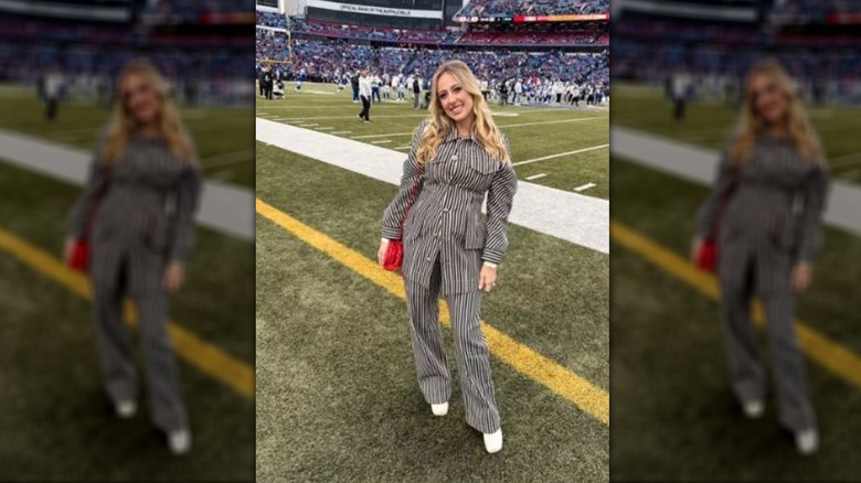 Brittany Mahomes standing on the sidelines of a football field in a striped set.