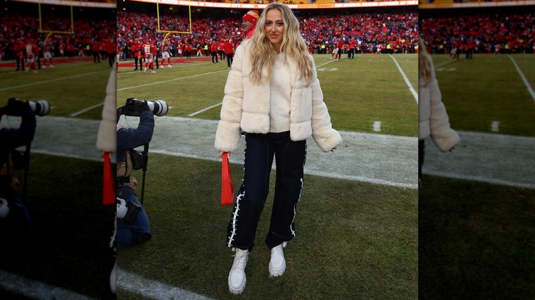 Brittany Mahomes poses in a white fuzzy jacket and black pants