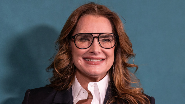 Brooke Shields smiling while wearing a suit and a pair of glasses.