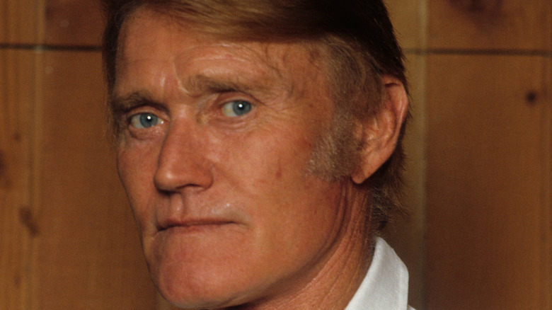 Close-up of Chuck Connors in front of a wooden background.