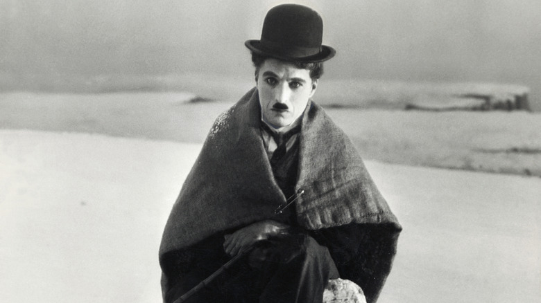 Charlie Chaplin sits wrapped in a blanket in the snow as The Lone Prospector in his 1925 film The Gold Rush.