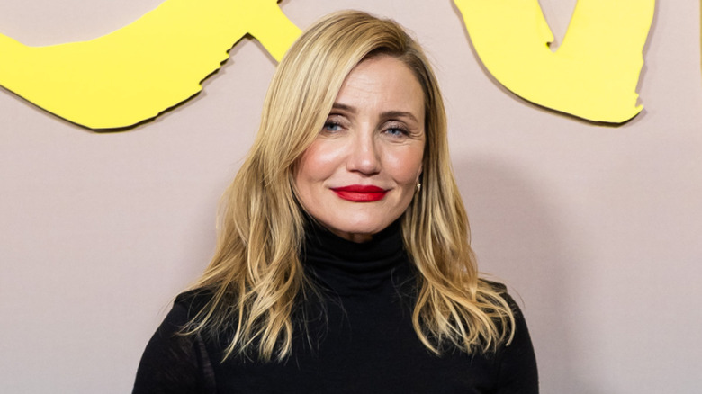 Cameron Diaz looking posing wearing a black top with her blonde hair down and wearing red lipstick.