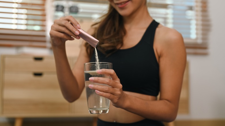 woman pouring collagen powder into drink