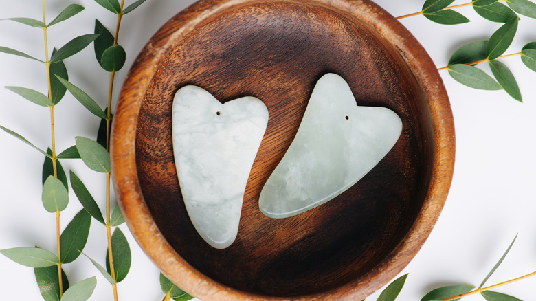 Two gua sha stones in a wooden bowl
