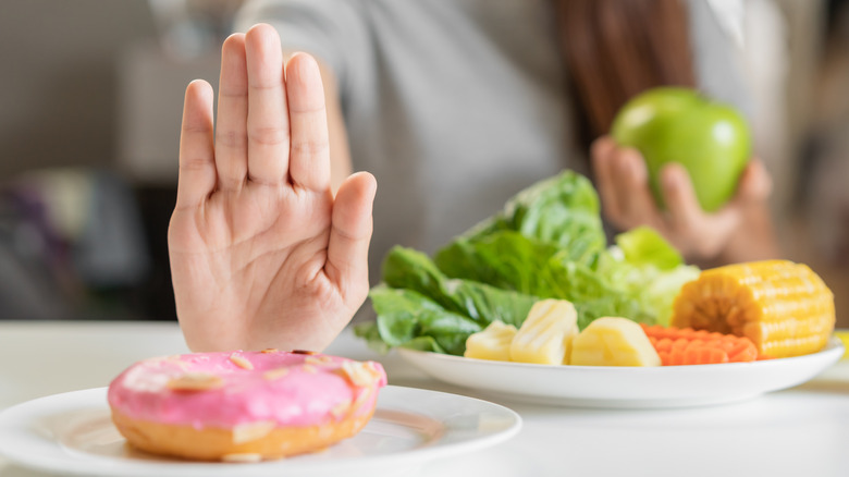 A woman rejecting a donut and eating veggies instead