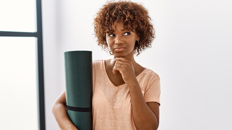 Woman thinking while holding yoga mat