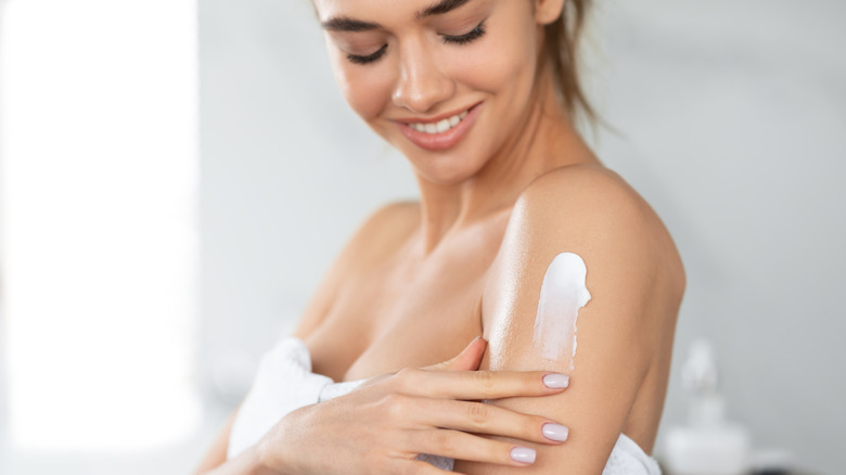 A woman putting body lotion on after taking a shower 