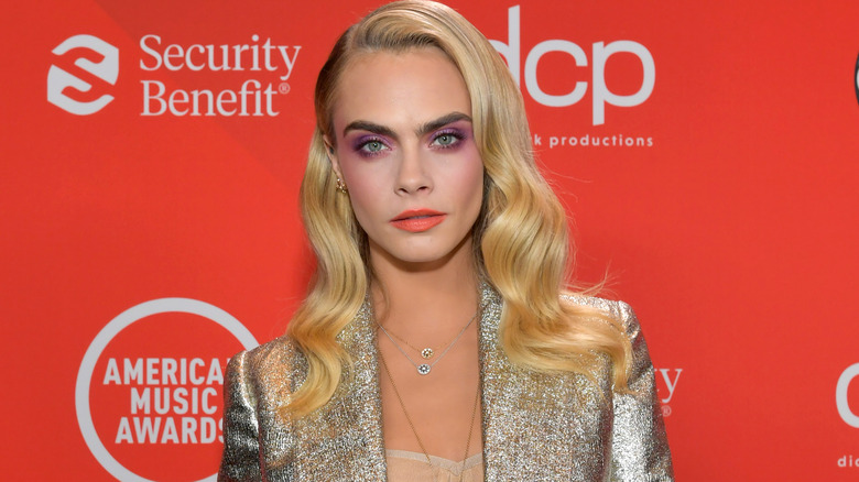 Cara Delevingne wears a silver blazer with curled blonde hair.