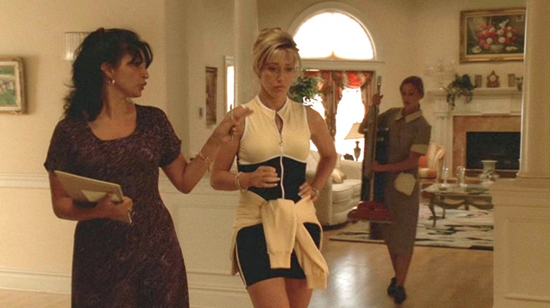 Carmela walking through house in yellow and black outfit