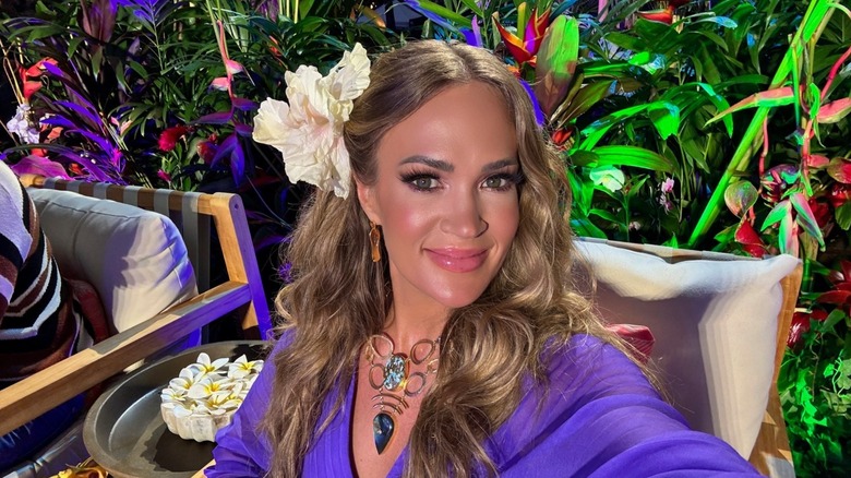 Carrie Underwood smiling with a large white flower in her hair.