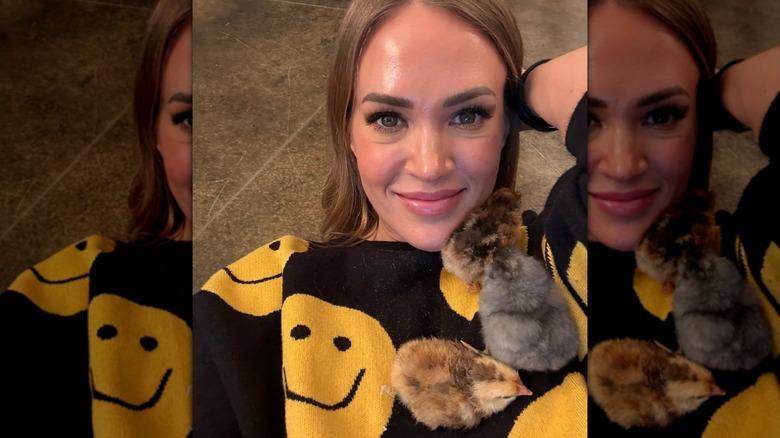 Carrie Underwood smiling with chicks crawling on her sweater.