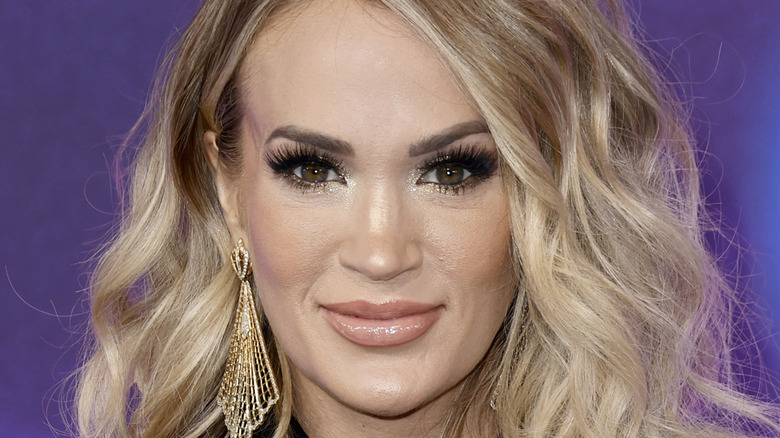 Carrie Underwood smiling and wearing large gold fan-shaped earrings.