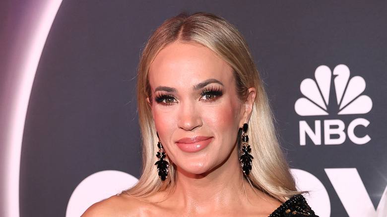 Carrie Underwood smiling in a black dress with matching earrings