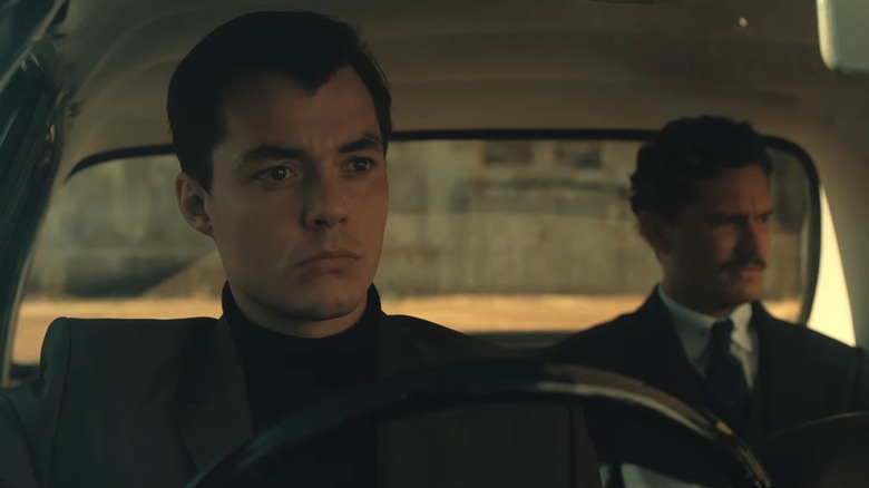 Jack Bannon in a turtleneck under a suit jacket, driving an old-timey car in Pennyworth