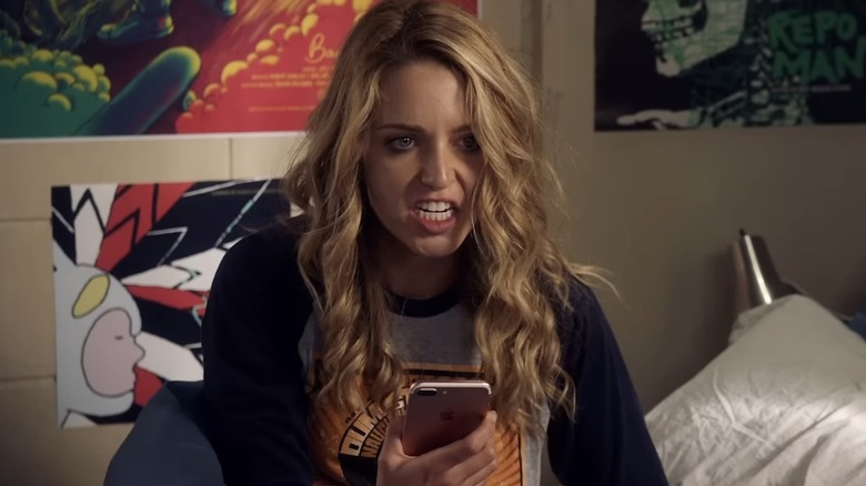 Jessica Rothe, mascara smudged and looking furious as she holds her phone in bed, in Happy Death Day 2U