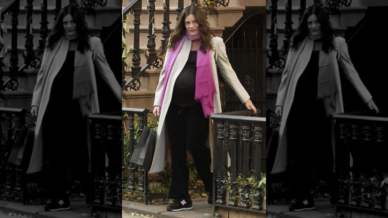 Pregnant Liv Tyler in all-black tracks, beige coat, and pink scarf