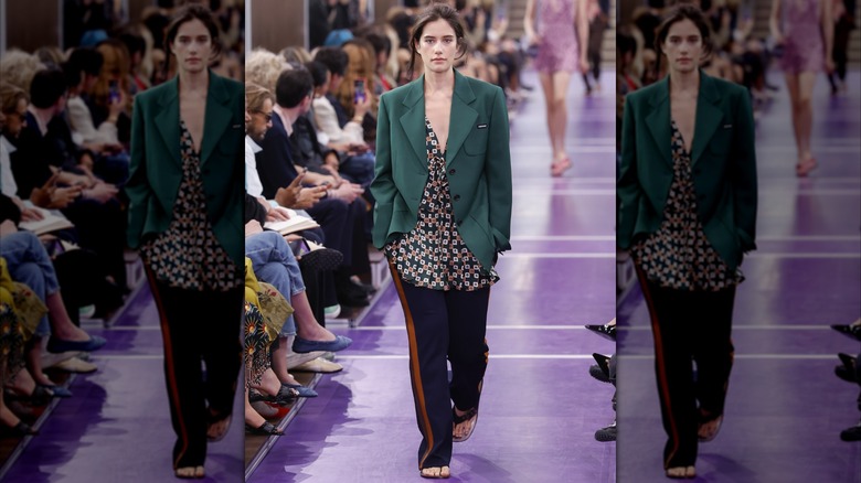 Ella Bleu Travolta walking on a runway wearing a blazer, shirt, and pants