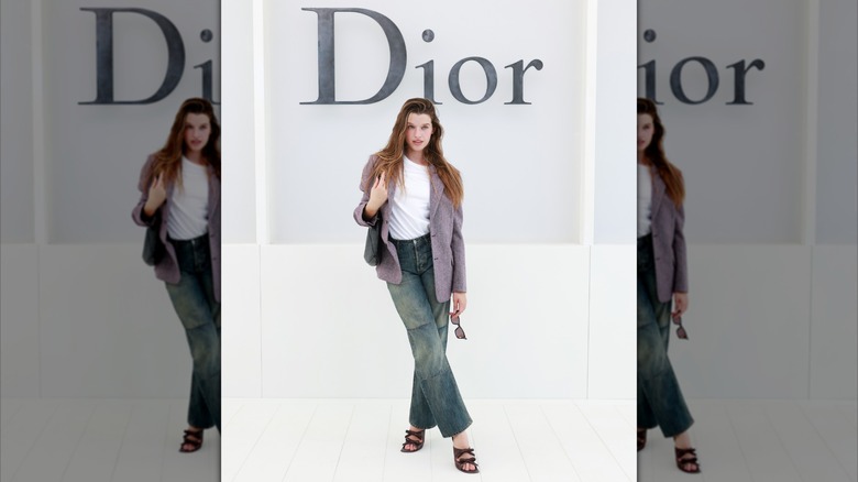 Ever Anderson wearing jeans and a blazer while posing in front of a Dior sign