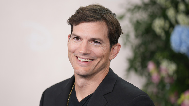 Ashton Kutcher smiles in front of a light background