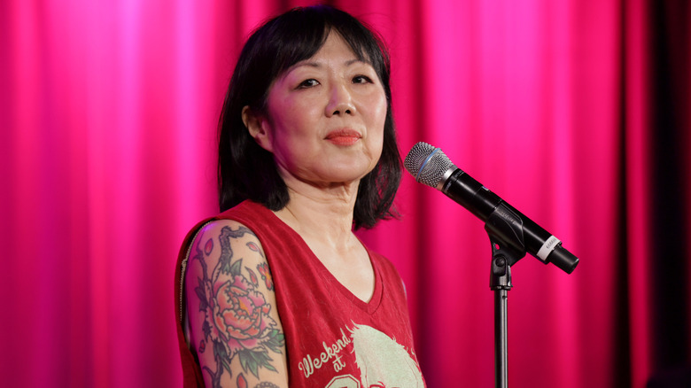 Margaret Cho speaking into a mic onstage in a red top