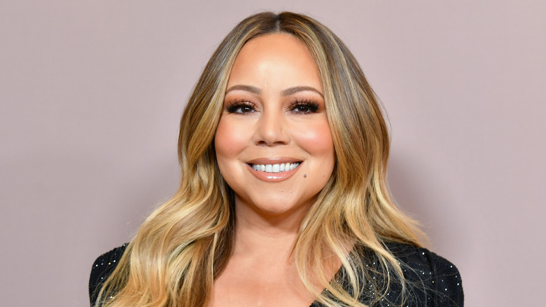 Mariah Carey in black shimmery dress against beige background