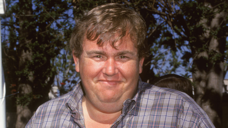John Candy smiling outdoors in a flannel shirt