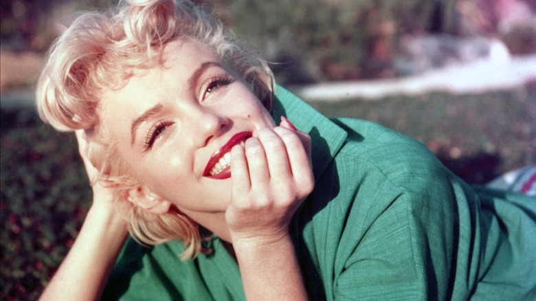 Marilyn Monroe smiling and posing outside for a photo in a green shirt