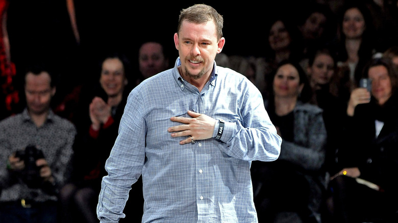 Alexander McQueen in a checked blue shirt as people behind applaud